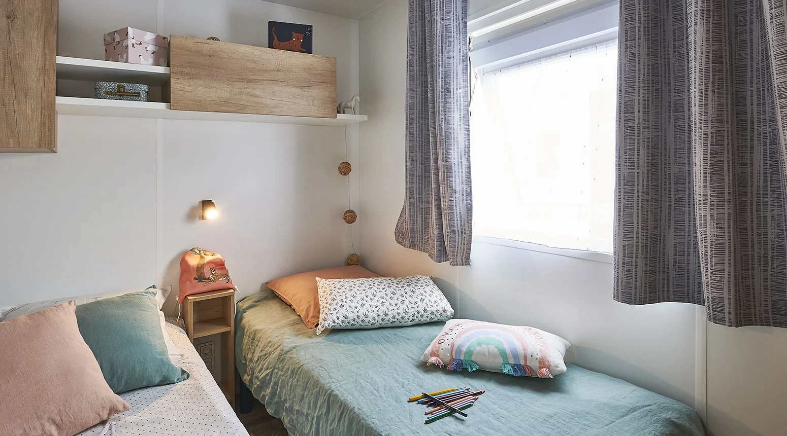 Chambre avec deux lits simples côte à côte, séparés par une petite table de chevet, et rangements en hauteur.