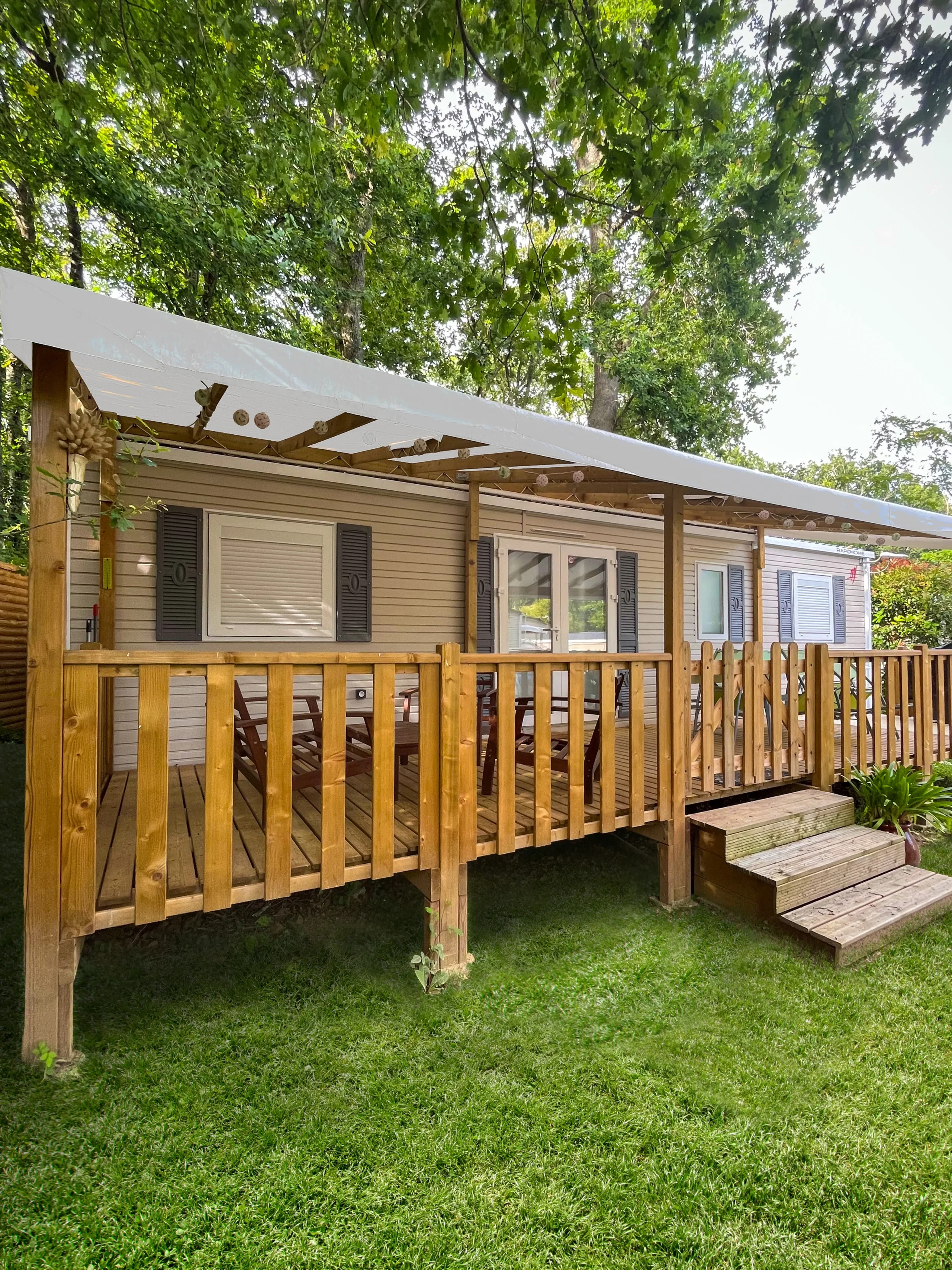 Mobil-home entouré d’arbres au Camping le ruisseau, hébergement insolite vers Biarritz avec terrasse en bois couverte.