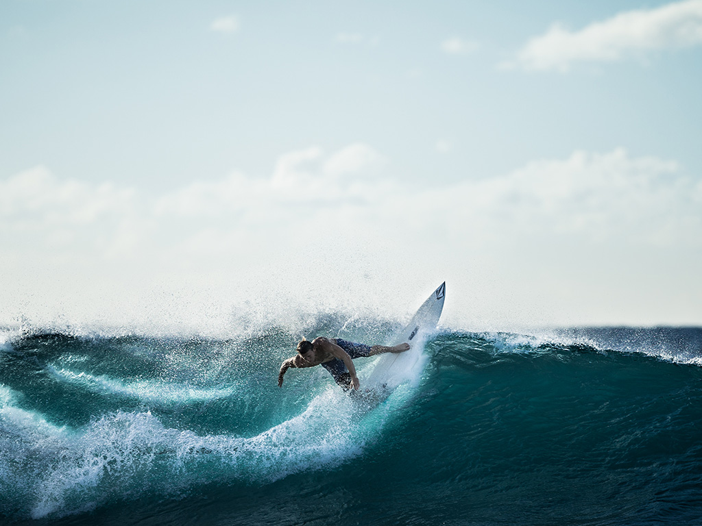 Surfeur effectuant un virage au sommet d’une vague, la planche redressée dans une gerbe d’eau.