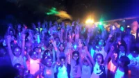 Les participants lèvent les bras sous les lumières colorées lors d’une soirée fluorescente au Camping le ruisseau, camping avec piscine proche de Biarritz.
