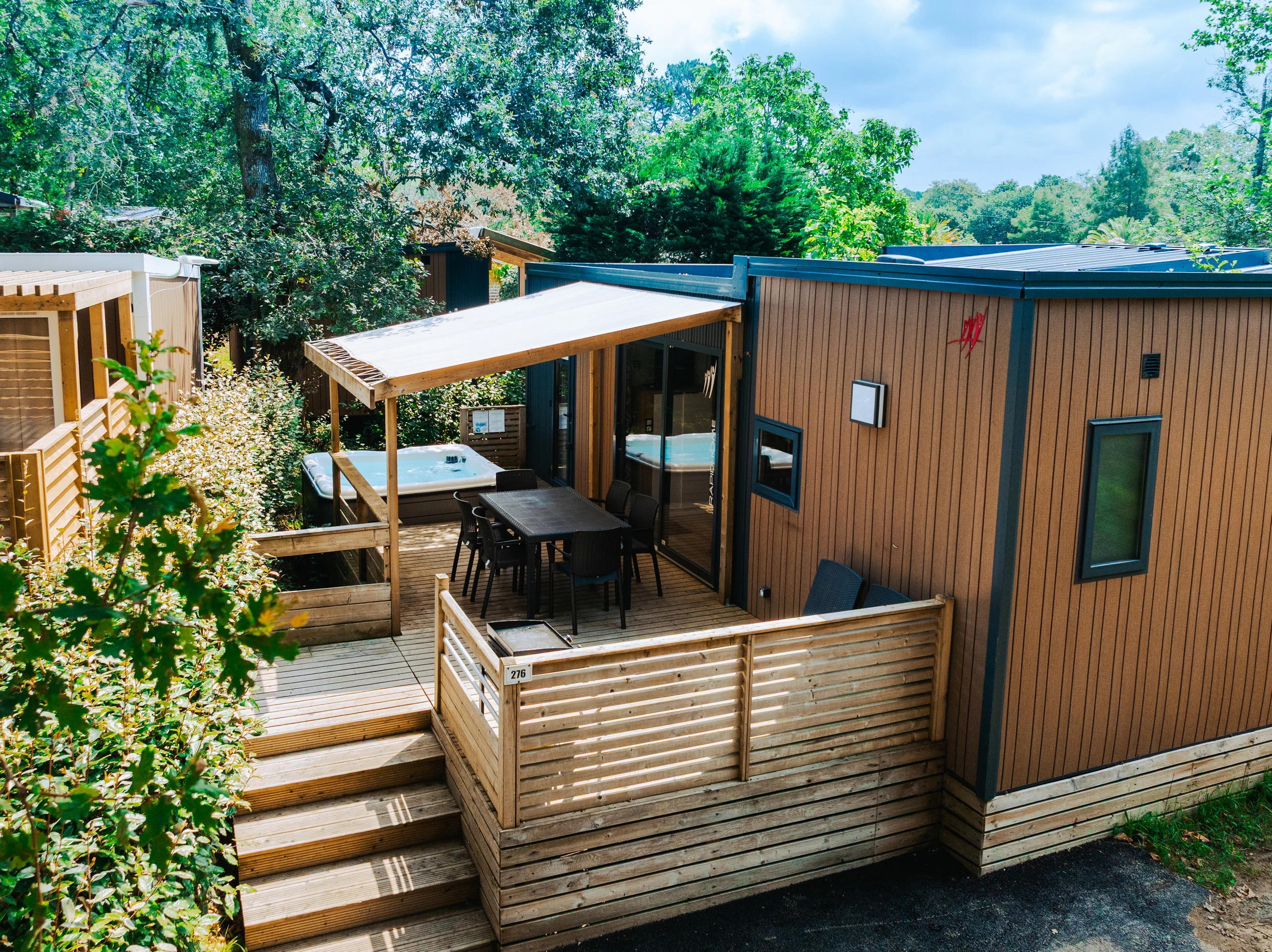 Terrasse en bois avec espace repas couvert et bain à remous d’un hébergement du Camping le ruisseau, camping 5 étoiles au Pays Basque.