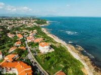 Vue aérienne d’un littoral rocheux bordé de maisons blanches aux toits de tuiles rouges.