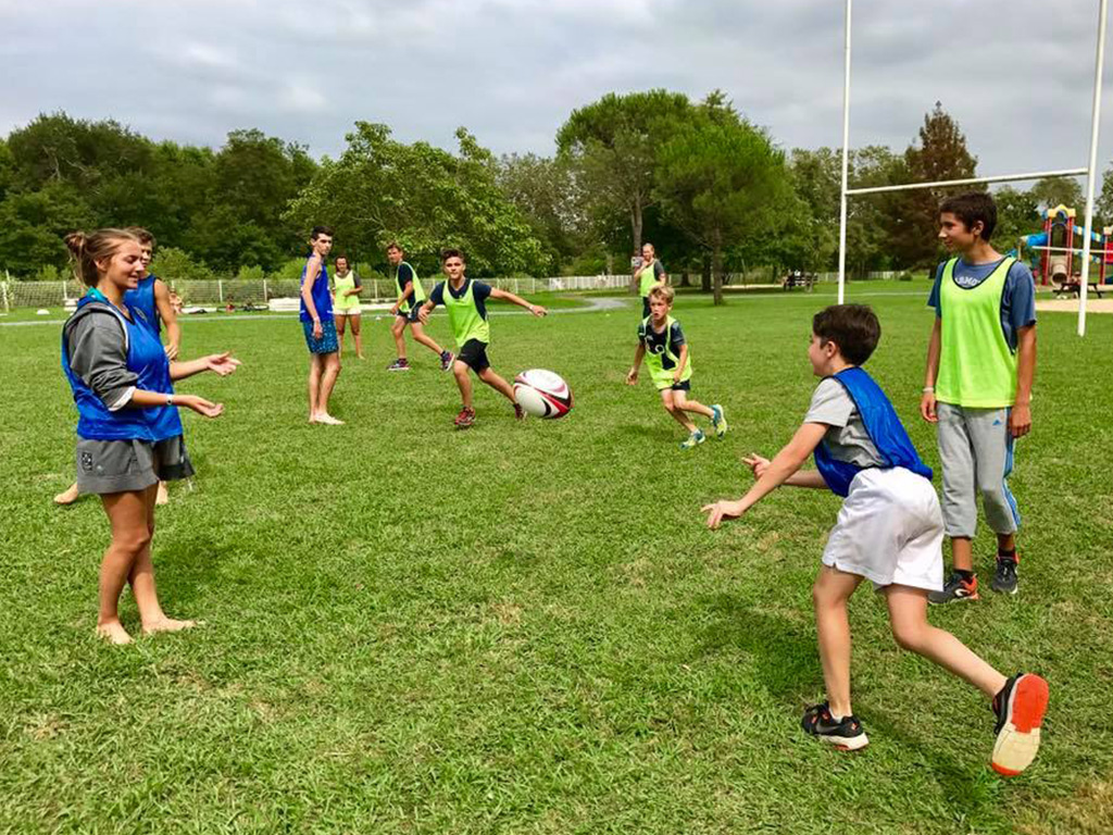 Jeunes en chasubles bleues et vertes jouant au rugby sur un terrain en herbe.