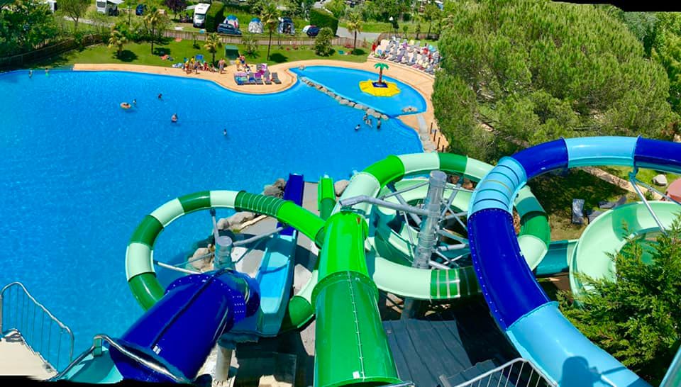 Toboggans aquatiques bleus et verts surplombant un grand bassin de baignade et un petit bassin avec jeux d’eau.