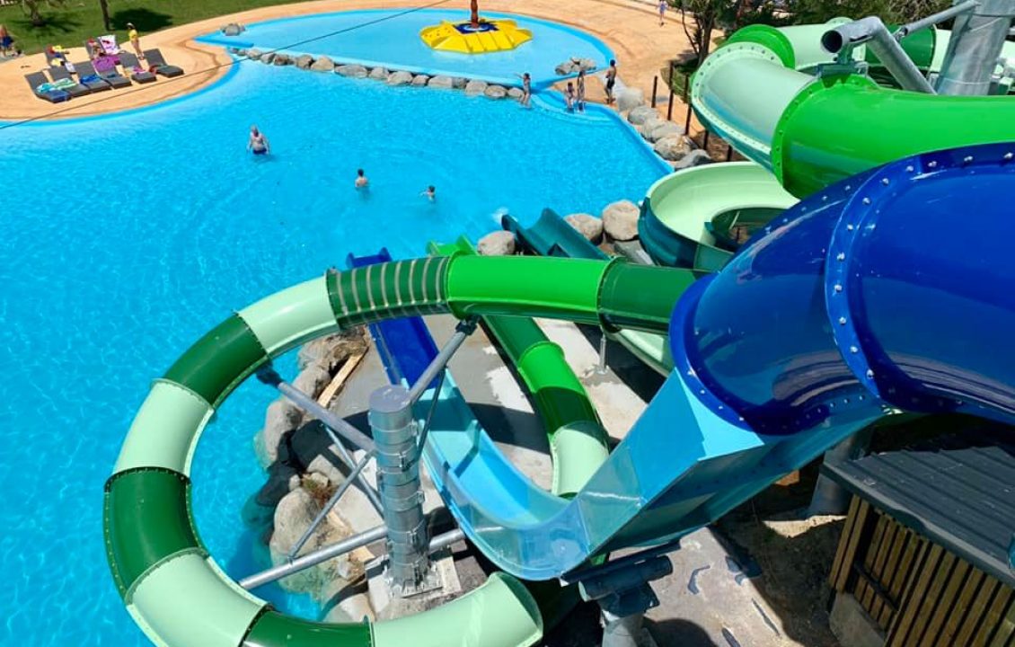 Vue d’ensemble des toboggans aquatiques en courbe, de la piscine et du bassin adjacent.