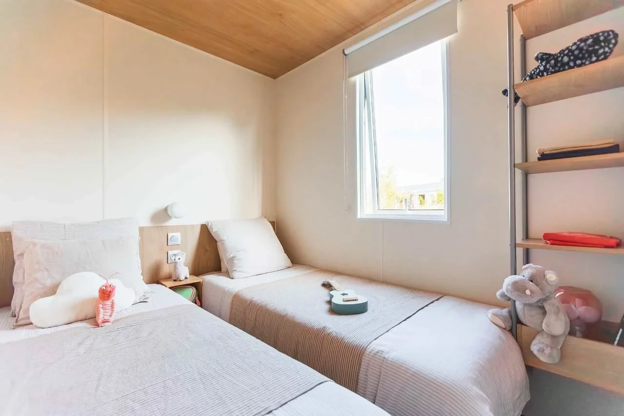 Chambre à deux lits simples avec peluches et rangements ouverts au Camping le ruisseau.