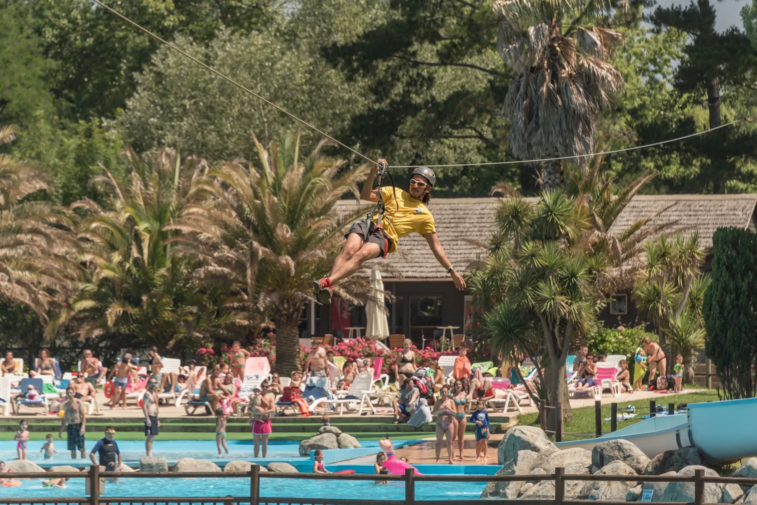 Un participant en tyrolienne au-dessus des bassins du Camping le ruisseau, camping avec piscine proche de Biarritz.