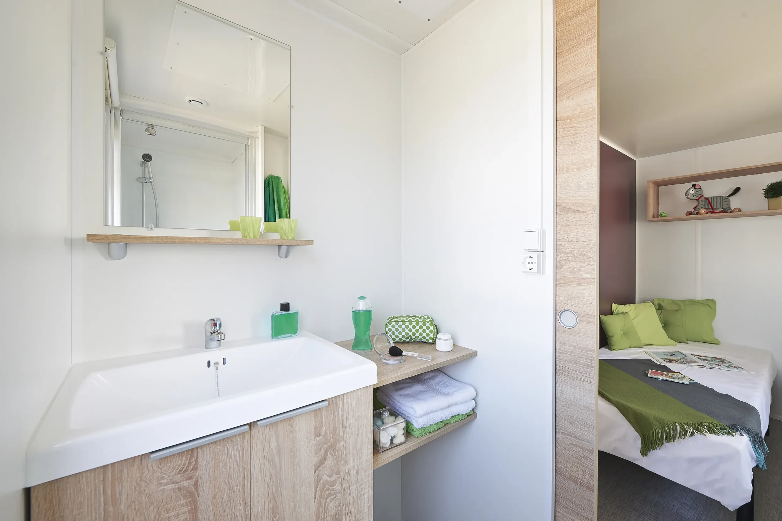 Salle d’eau avec vasque, miroir et rangements, ouverte sur une chambre avec lit double.