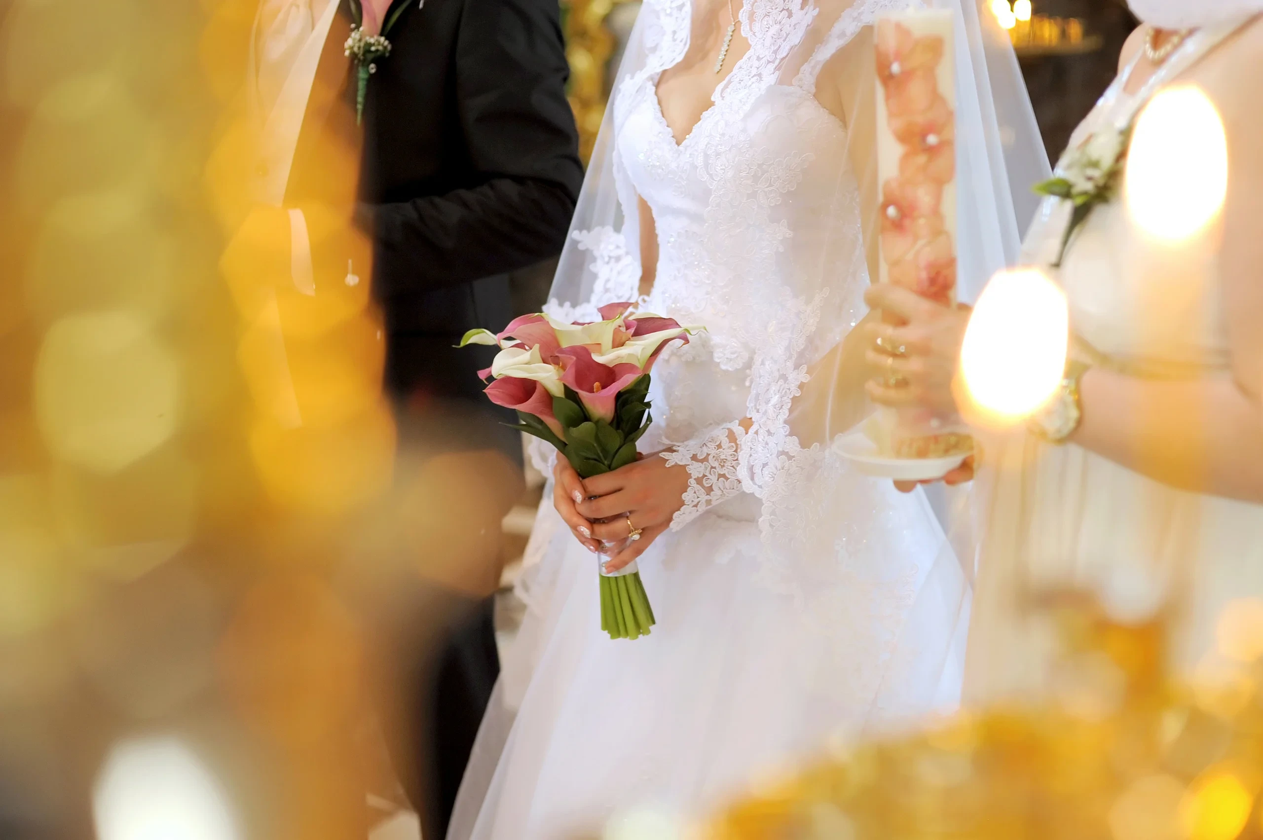 Mariée en robe de dentelle blanche tenant un bouquet de fleurs roses et blanches, près du marié.