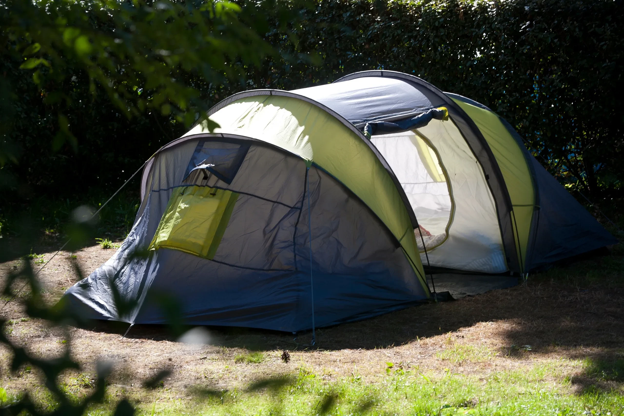 Tente à plusieurs arceaux avec auvent, installée sur un emplacement arboré du Camping le ruisseau.