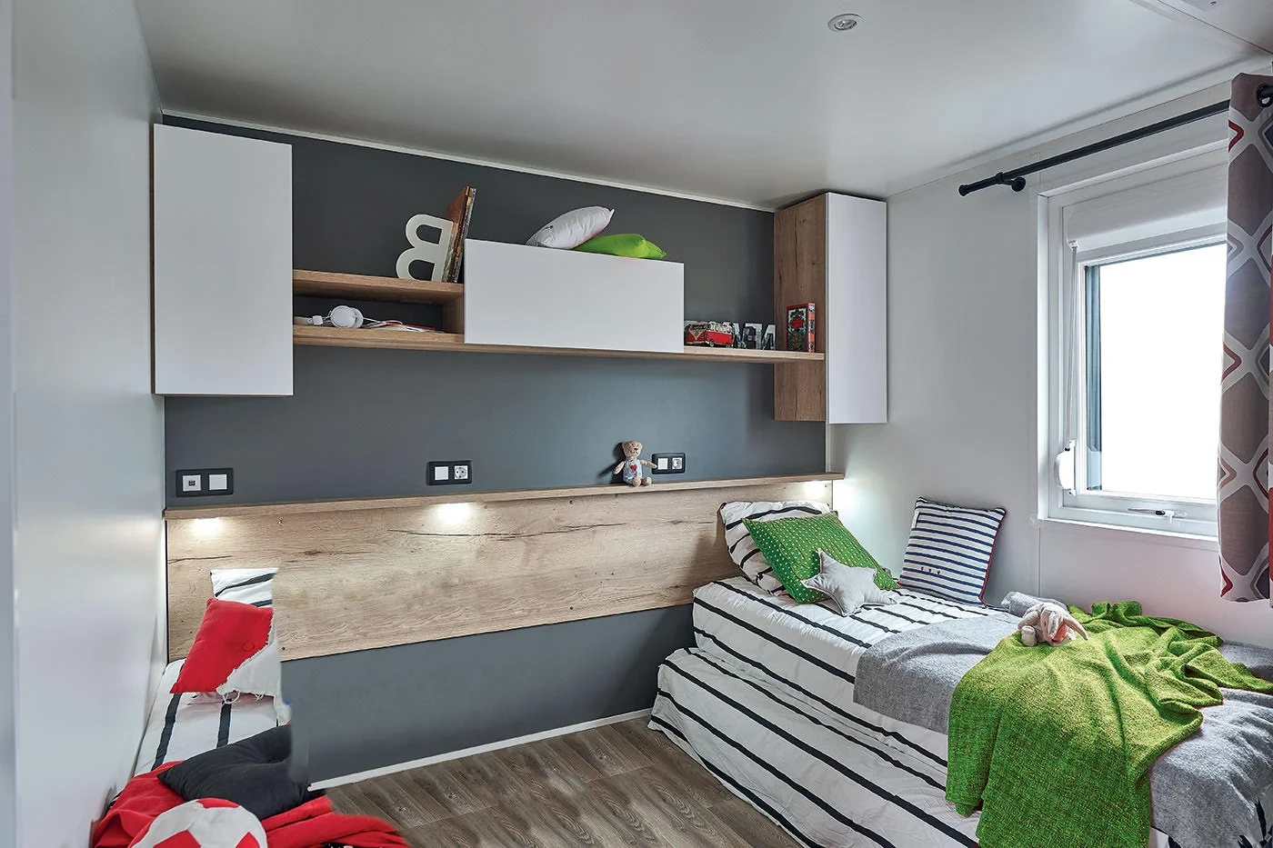 Chambre avec deux lits simples, rangements muraux et fenêtre.