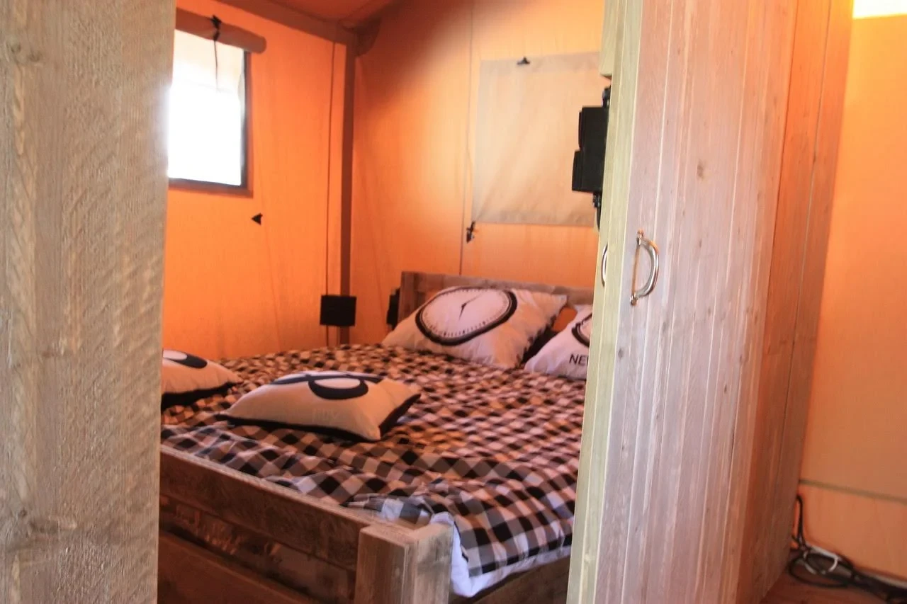 Chambre d’un hébergement insolite vers Biarritz, avec lit double en bois et parois en toile orange.