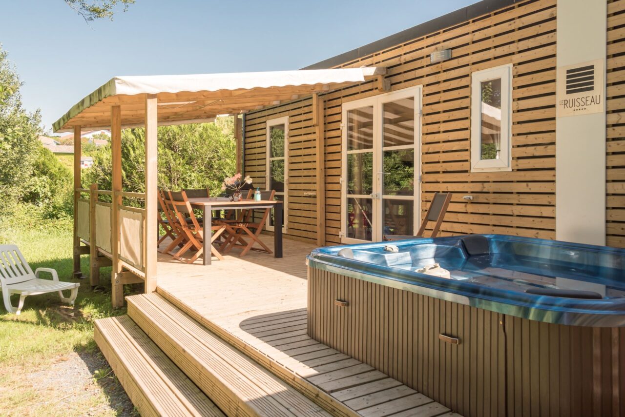 Spa privatif sur la terrasse en bois d’un hébergement du Camping le ruisseau, avec coin repas couvert.