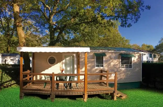 Mobil-home du Camping le ruisseau, hébergement insolite vers Biarritz, avec terrasse en bois couverte aménagée d’une table et de chaises.