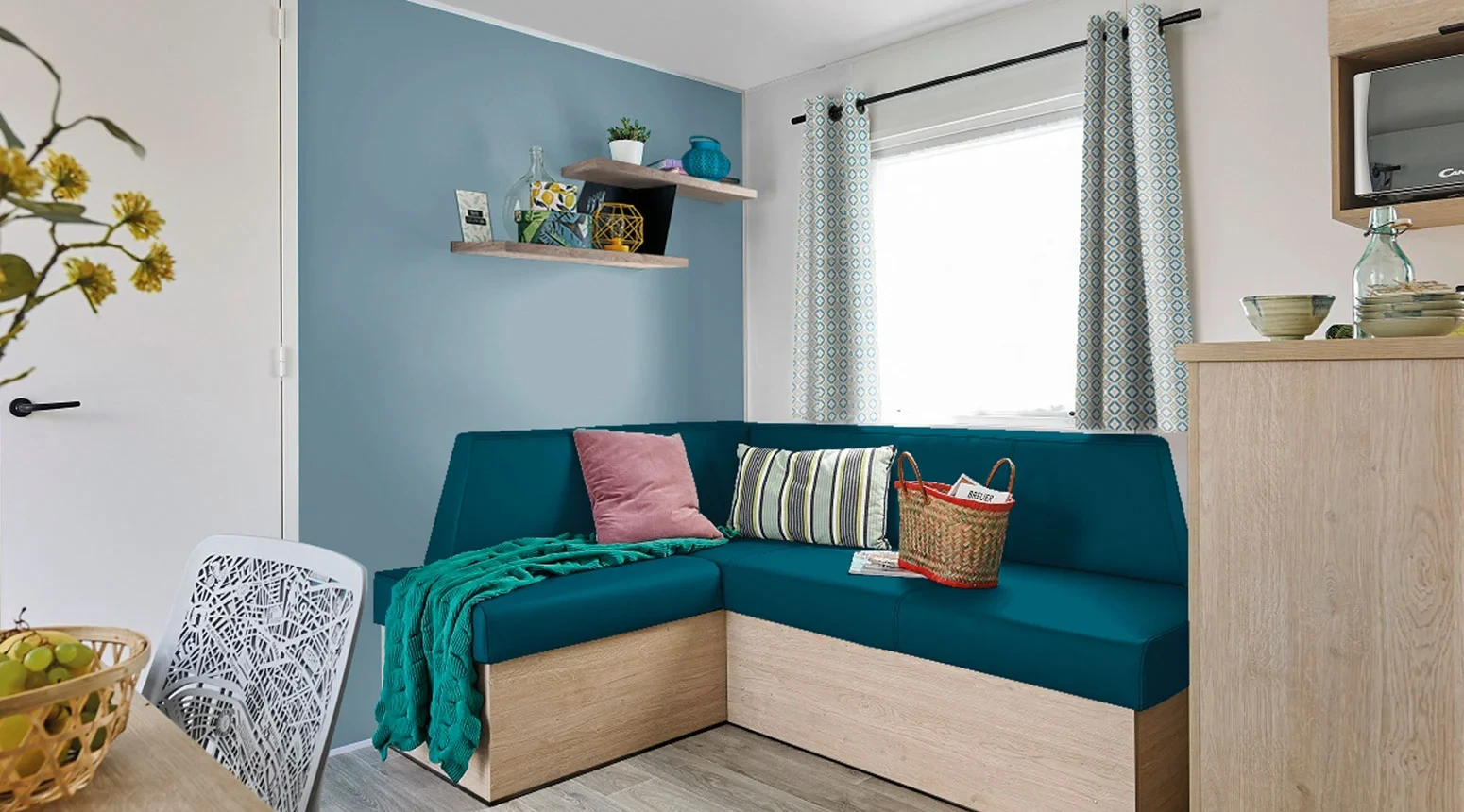 Salon avec banquette d’angle bleu canard sous la fenêtre et mur bleu clair.