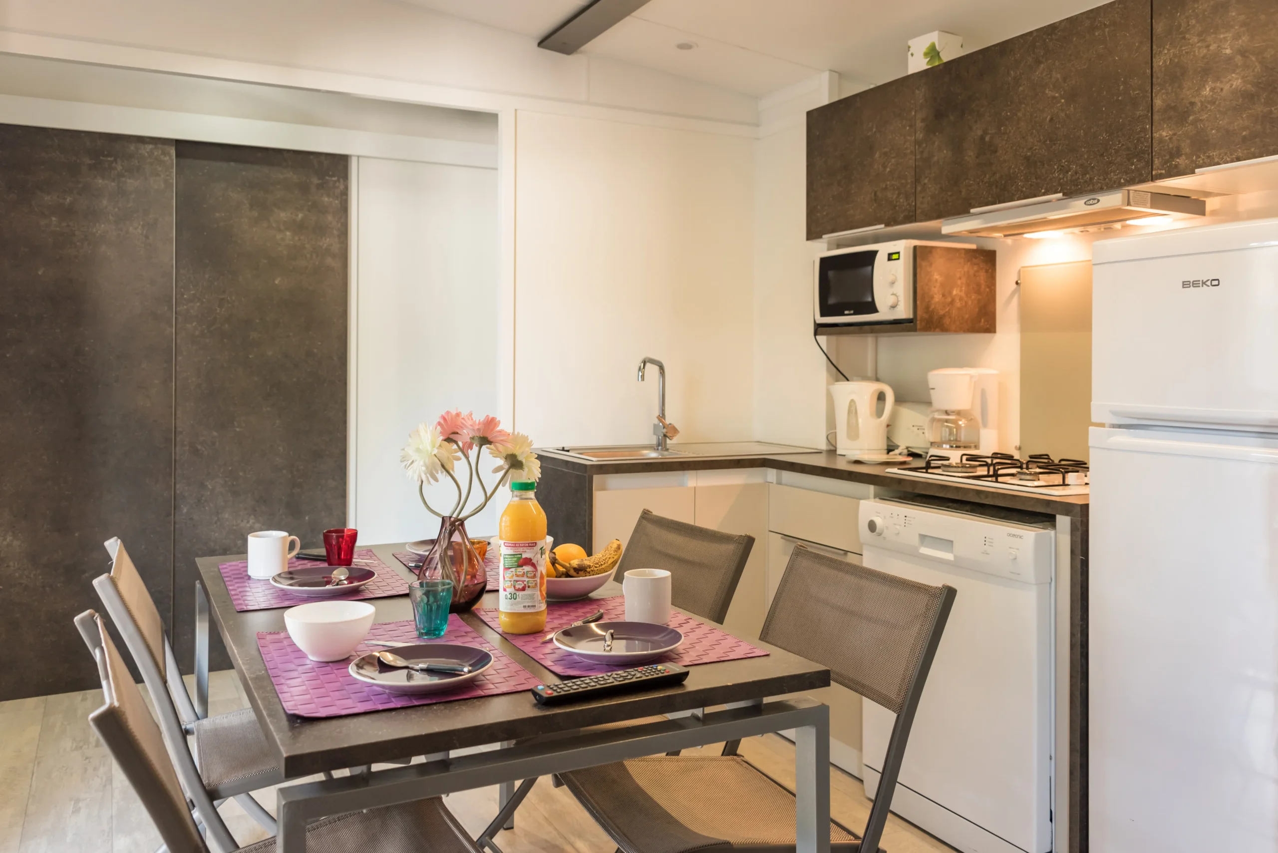 Cuisine en angle équipée et table dressée pour quatre personnes dans l’hébergement.