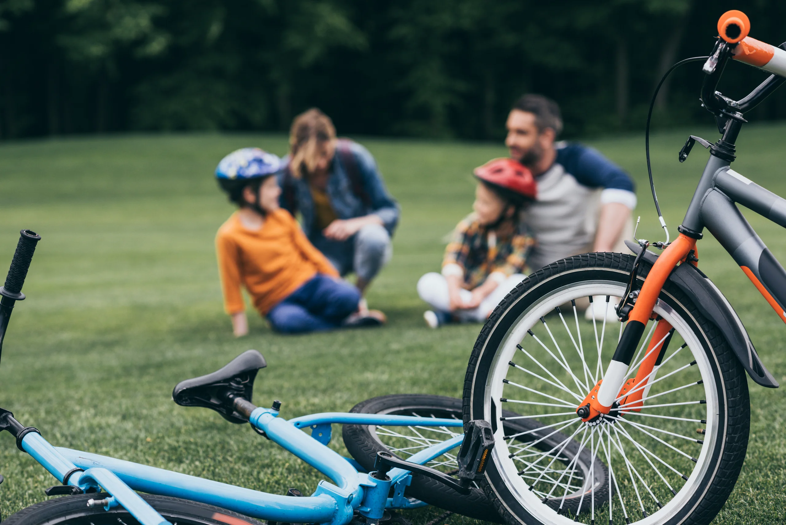 Vélos au premier plan et famille assise dans l’herbe à l’arrière-plan, avec deux enfants casqués.