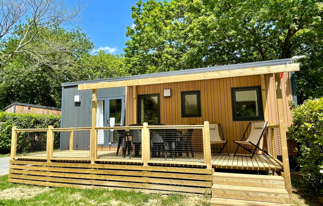 Mobil-home du Camping le ruisseau avec terrasse surélevée, garde-corps et fauteuils pliants.