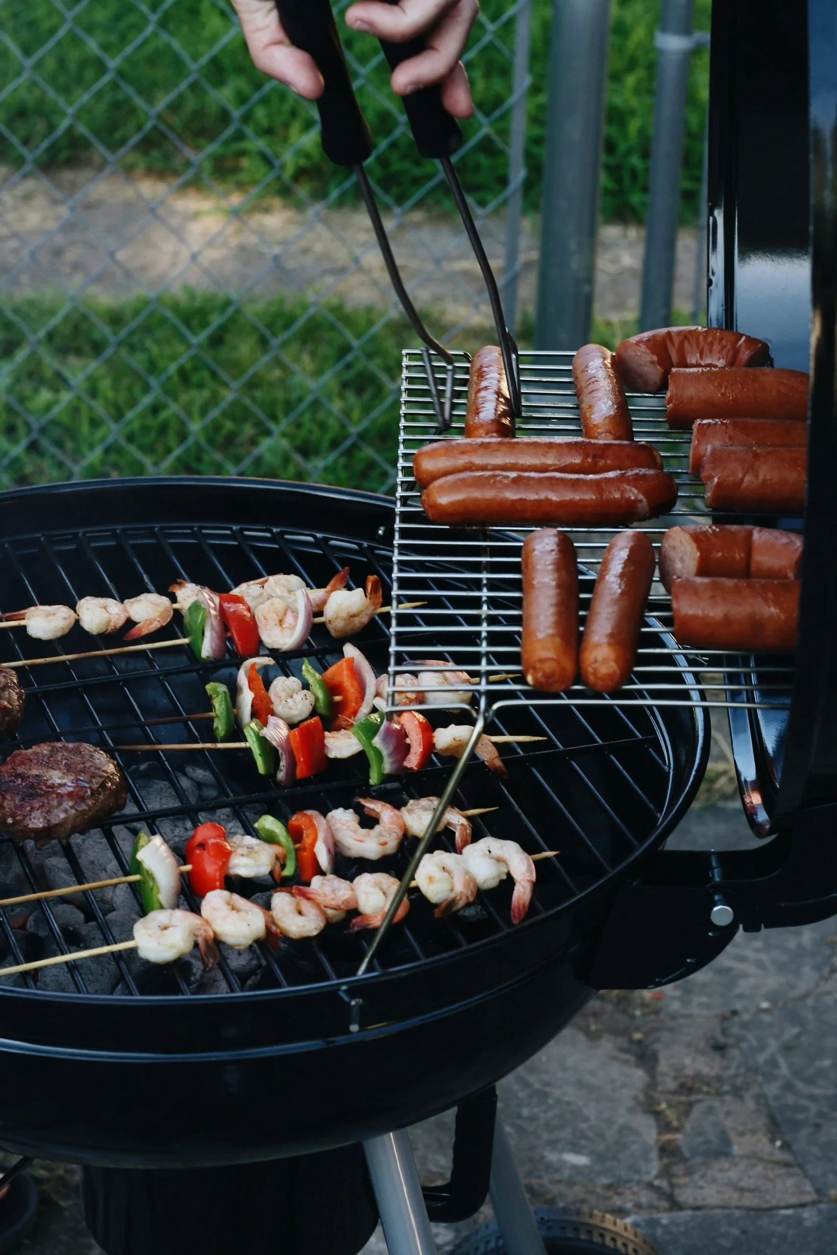 Saucisses et brochettes de crevettes et de légumes sur les grilles d’un barbecue.