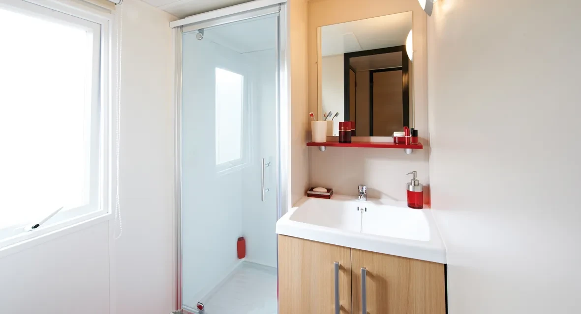 Salle d’eau avec cabine de douche vitrée, vasque sur meuble en bois et miroir.