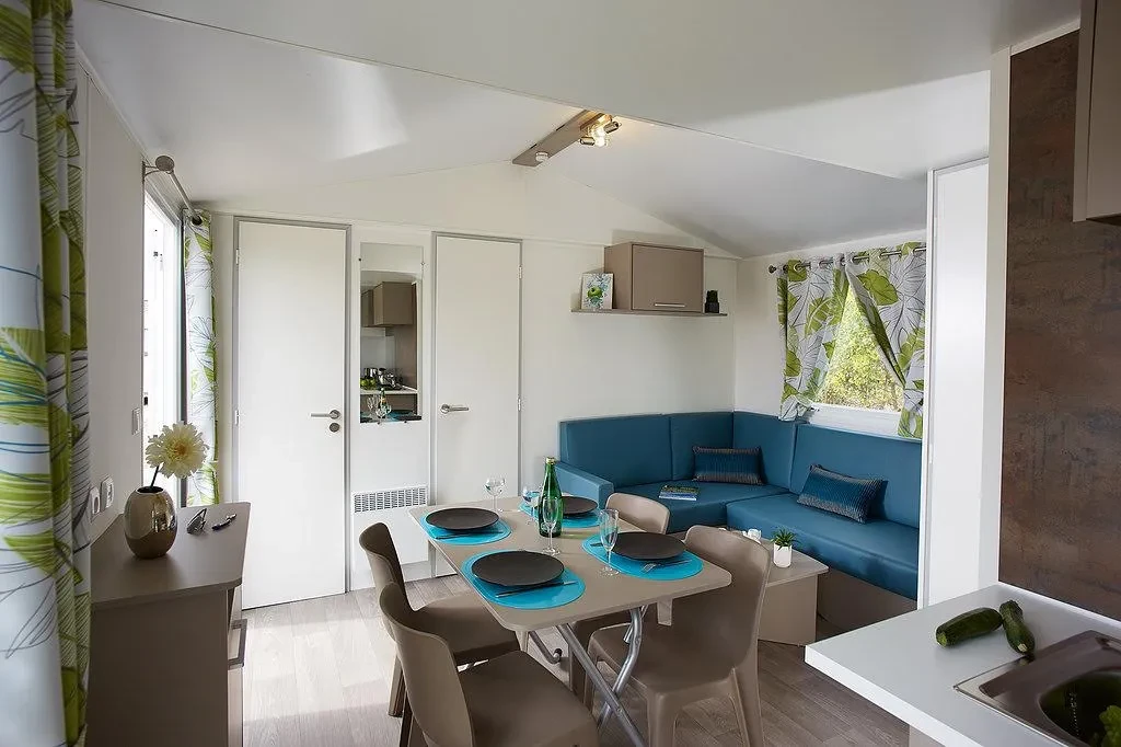 Séjour du Camping le ruisseau avec banquette d’angle bleue et table dressée pour quatre personnes.