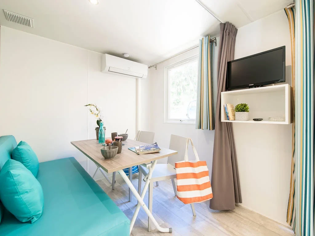 Séjour du Camping le ruisseau avec banquette turquoise et table de repas près de la fenêtre.