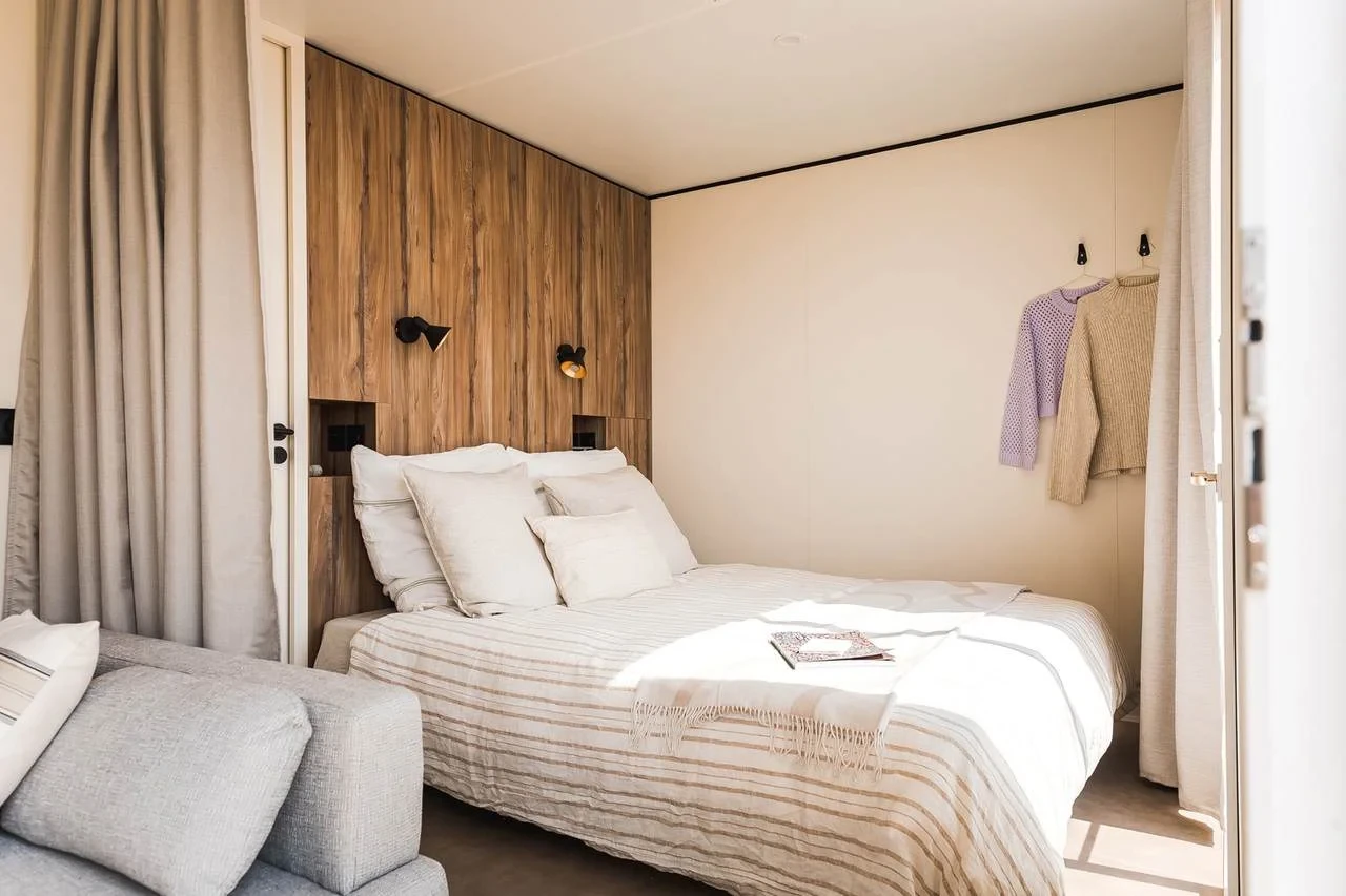 Lit double contre un mur habillé de bois, avec liseuses et niches intégrées, au Camping le ruisseau.