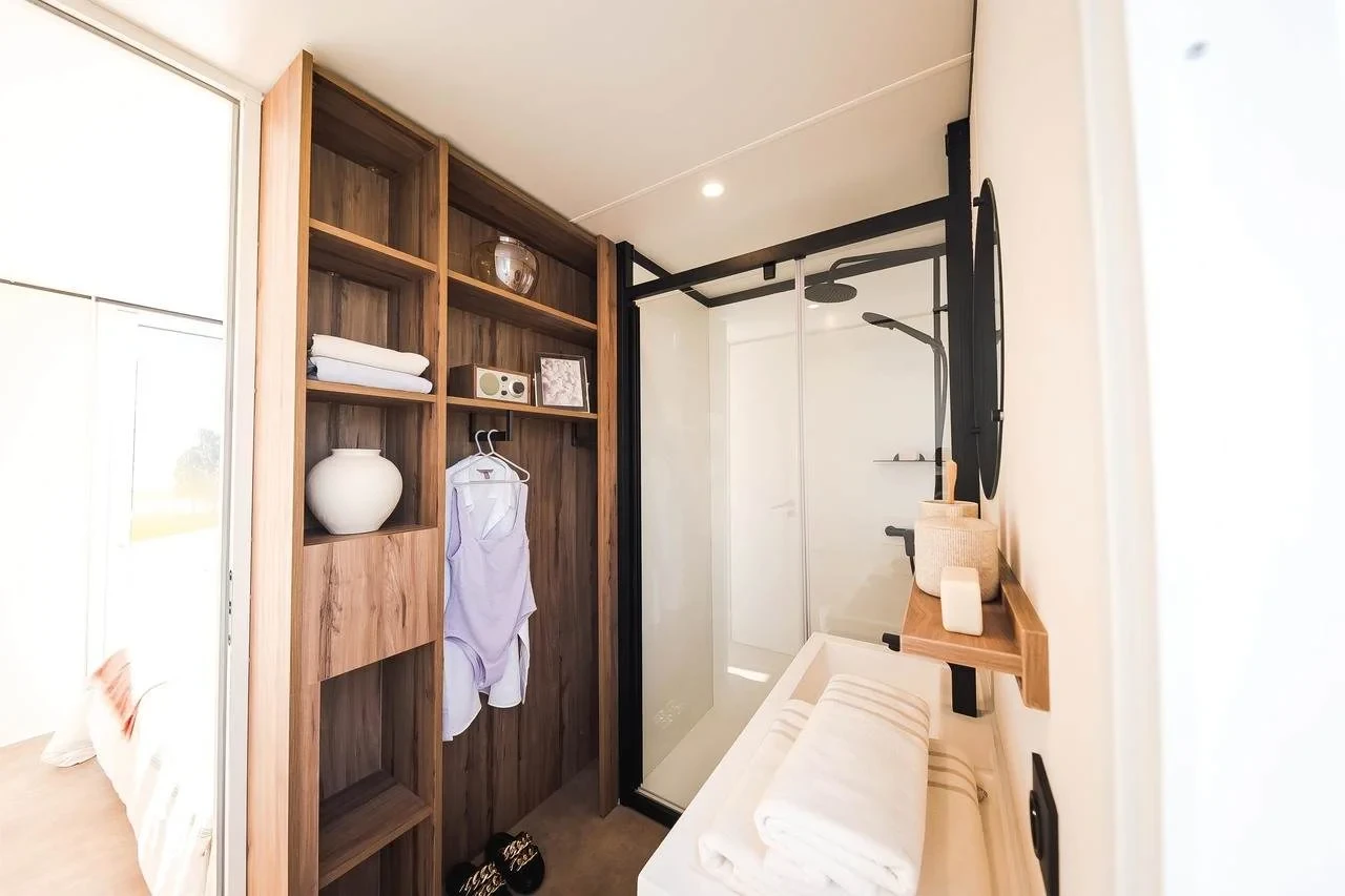 Dressing ouvert en bois à côté de la salle d’eau avec vasque et douche vitrée.