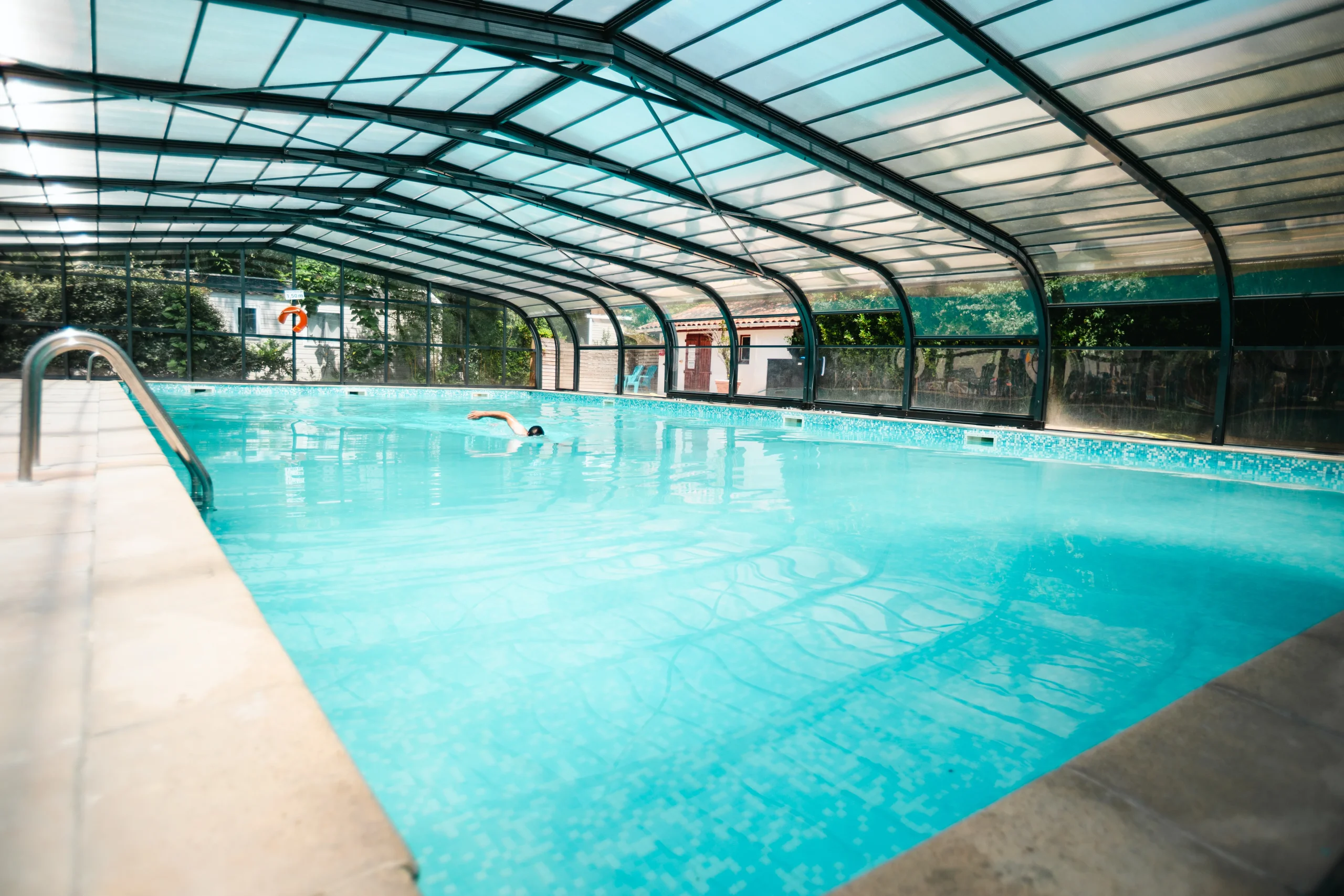 Une personne nage dans la piscine sous verrière du Camping le ruisseau, camping à Bidart.