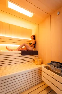 Une femme assise sur une banquette en bois dans le sauna du Camping le ruisseau, camping avec jacuzzi.