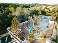 Vue aérienne de l’espace aquatique du Camping le ruisseau, camping à Bidart, avec bassins sinueux, palmiers et transats.