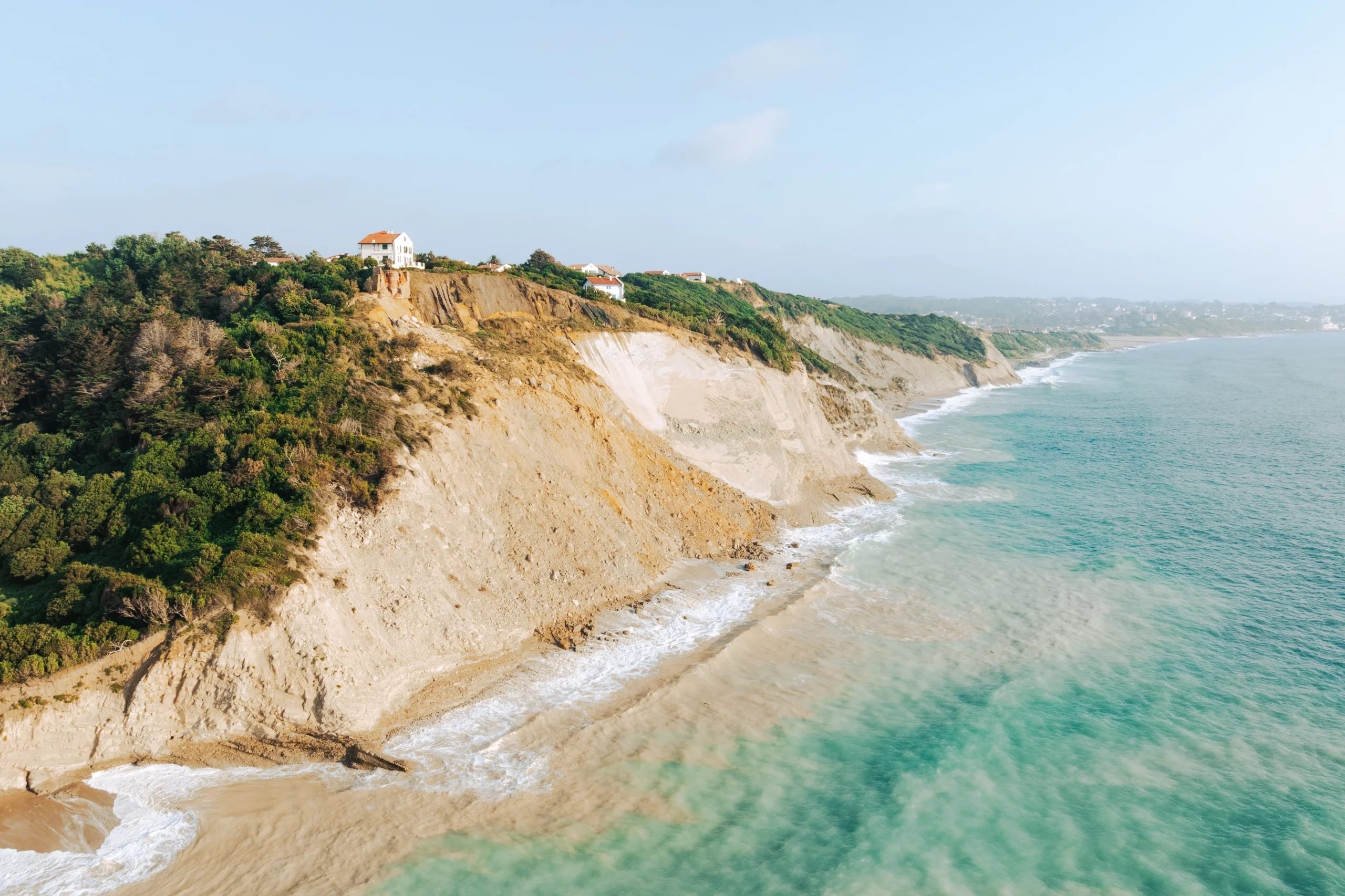 Falaises bordées de végétation et de maisons au-dessus de la mer turquoise.