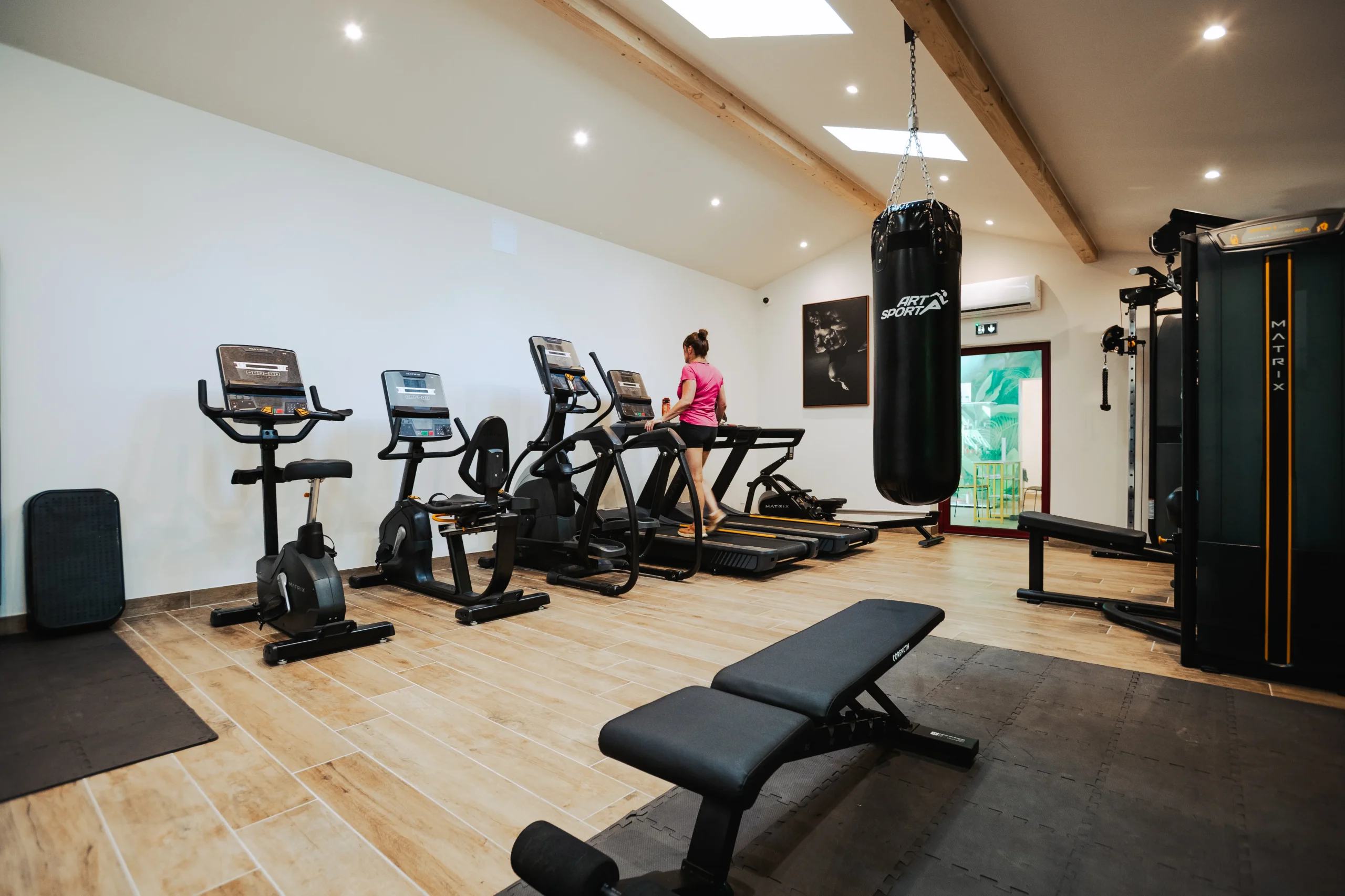 Appareils de cardio, banc de musculation et sac de frappe dans la salle de fitness du Camping le ruisseau, camping avec jacuzzi.