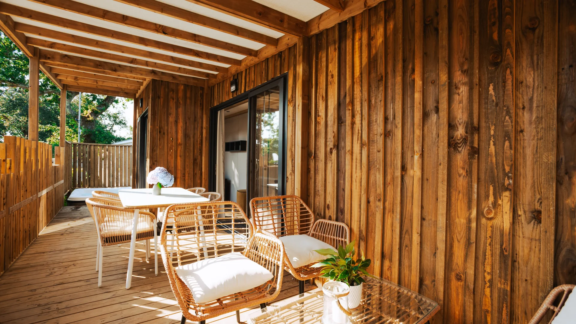 Terrasse couverte d’un hébergement insolite vers Biarritz au Camping le ruisseau, avec fauteuils en rotin et table de repas.