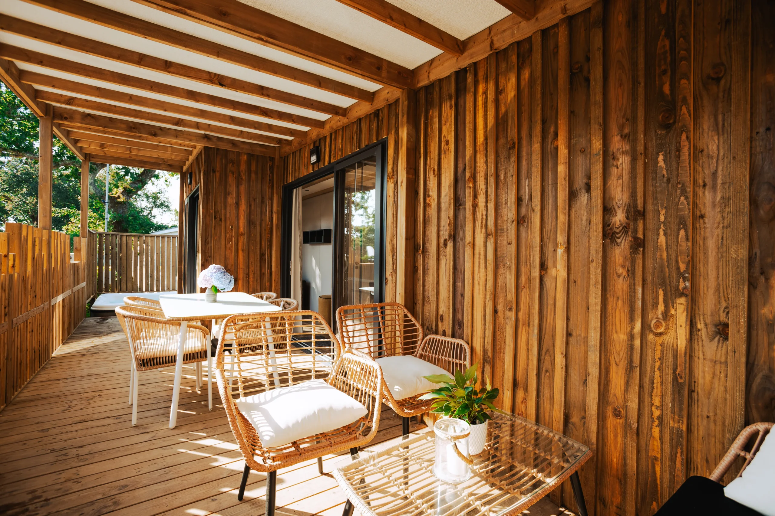 Terrasse couverte d’un hébergement insolite vers Biarritz au Camping le ruisseau, avec fauteuils en rotin et table de repas.
