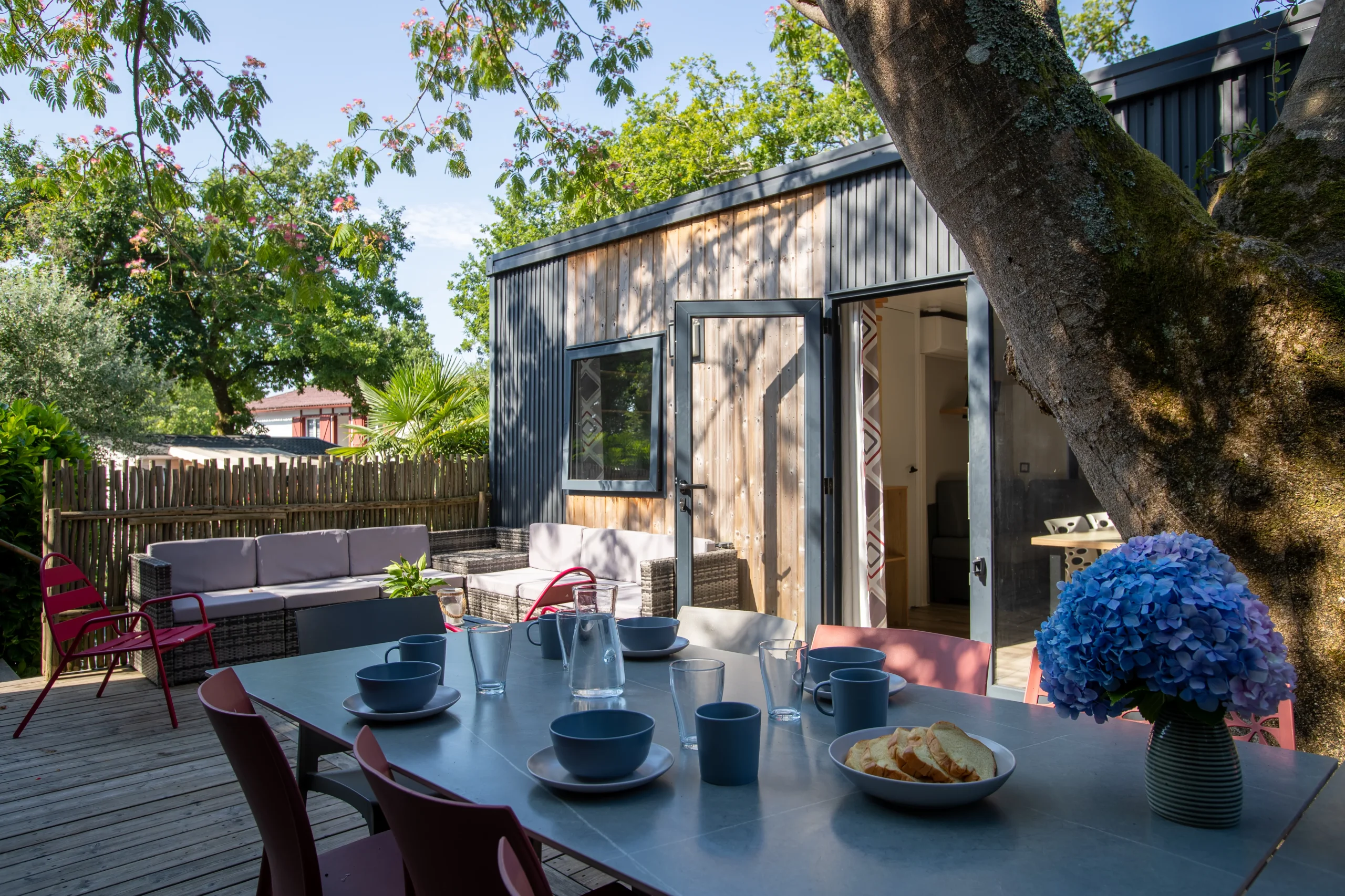 Terrasse arborée d’un hébergement insolite vers Biarritz au Camping le ruisseau, avec table dressée et salon extérieur.