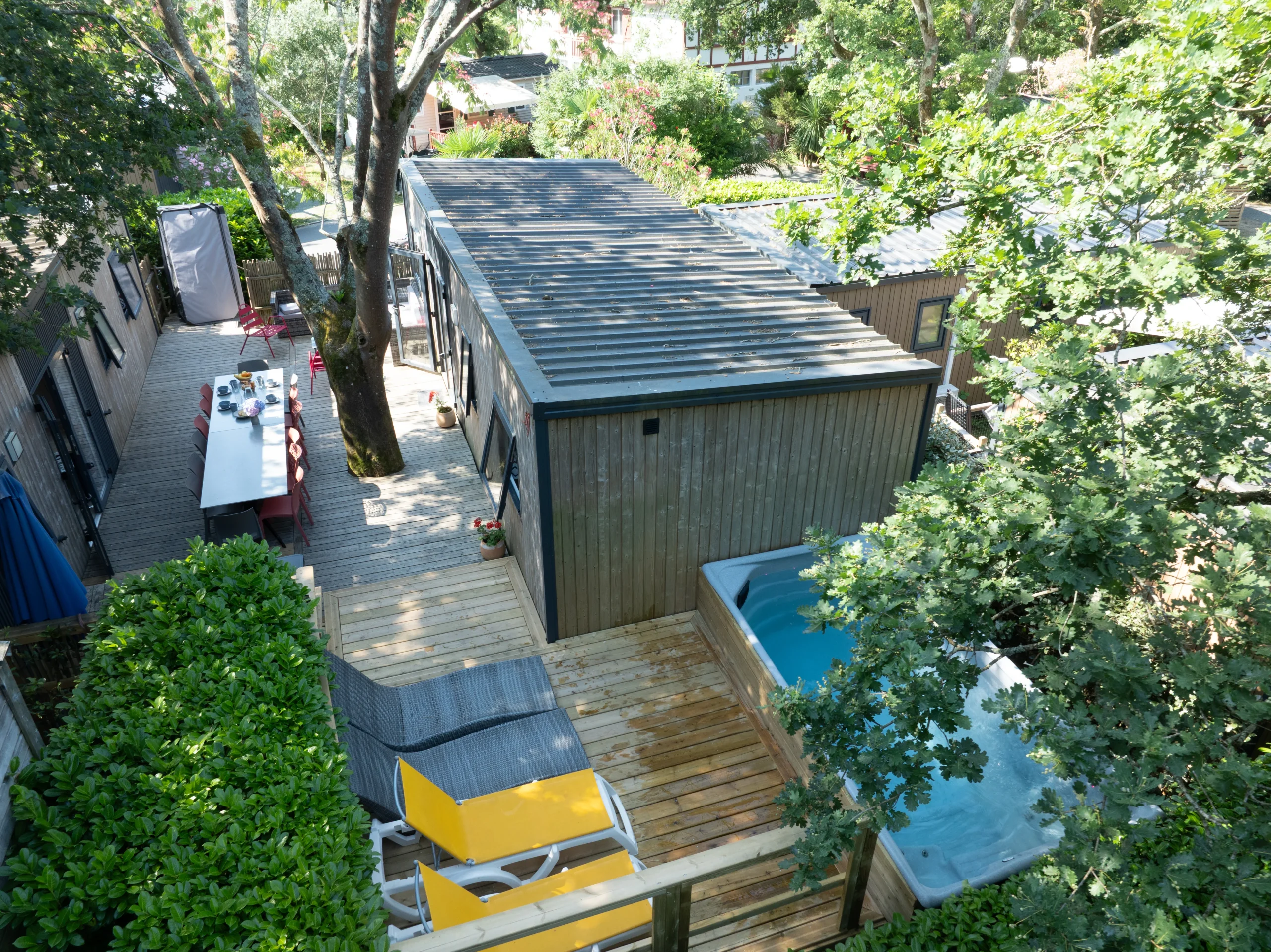 Vue en hauteur d’un hébergement insolite vers Biarritz au Camping le ruisseau, avec terrasse arborée, espace repas, transats et bassin à remous.
