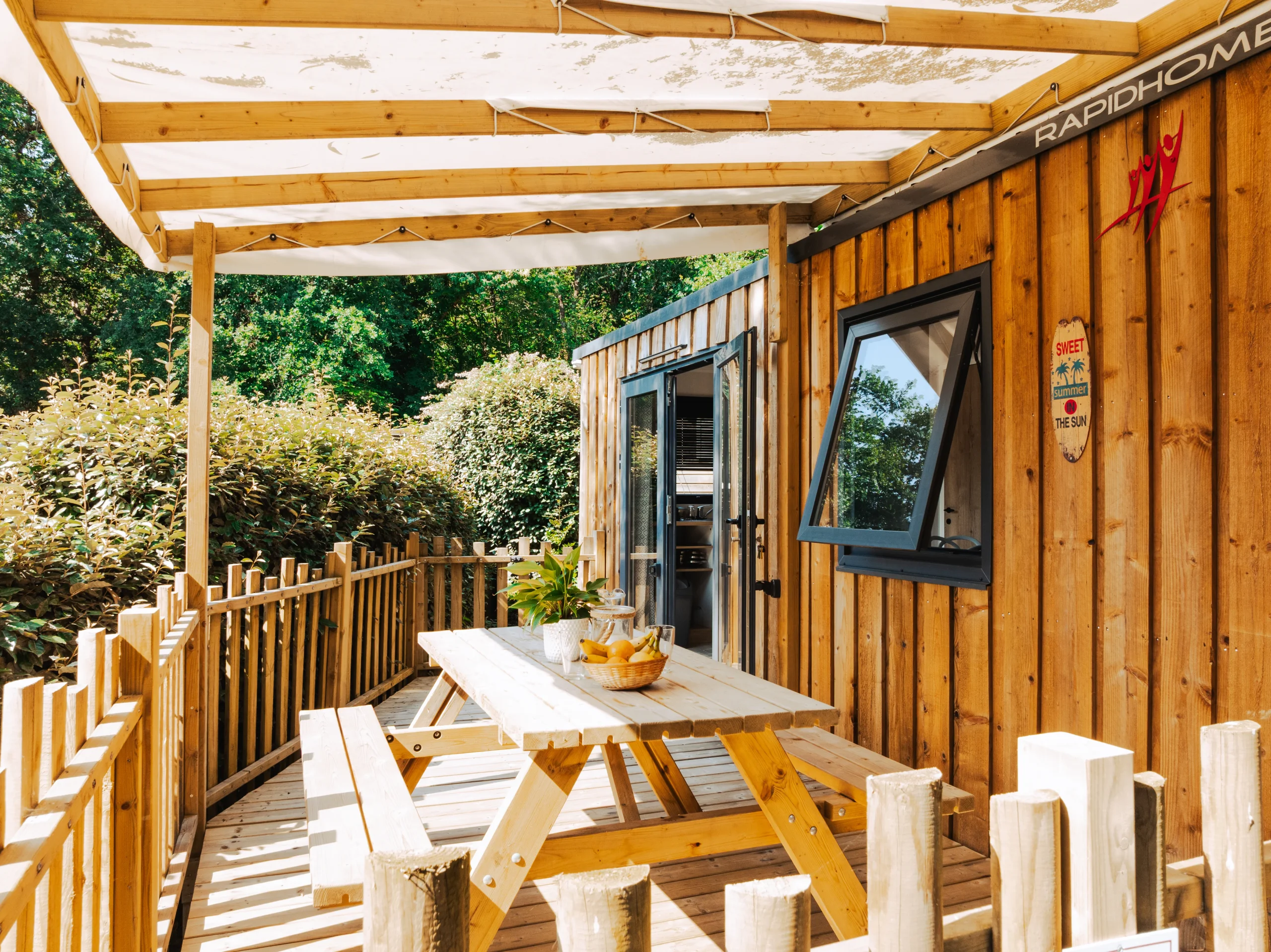 Terrasse couverte d’un mobil-home du Camping le ruisseau, camping à Bidart, avec table et bancs en bois.