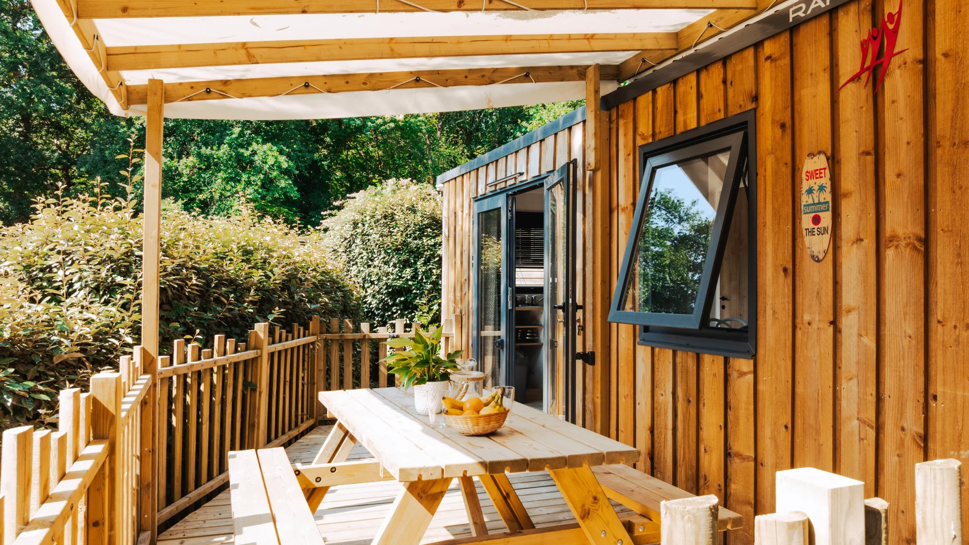 Terrasse en bois couverte d’une toile, avec table de pique-nique devant la cabane.