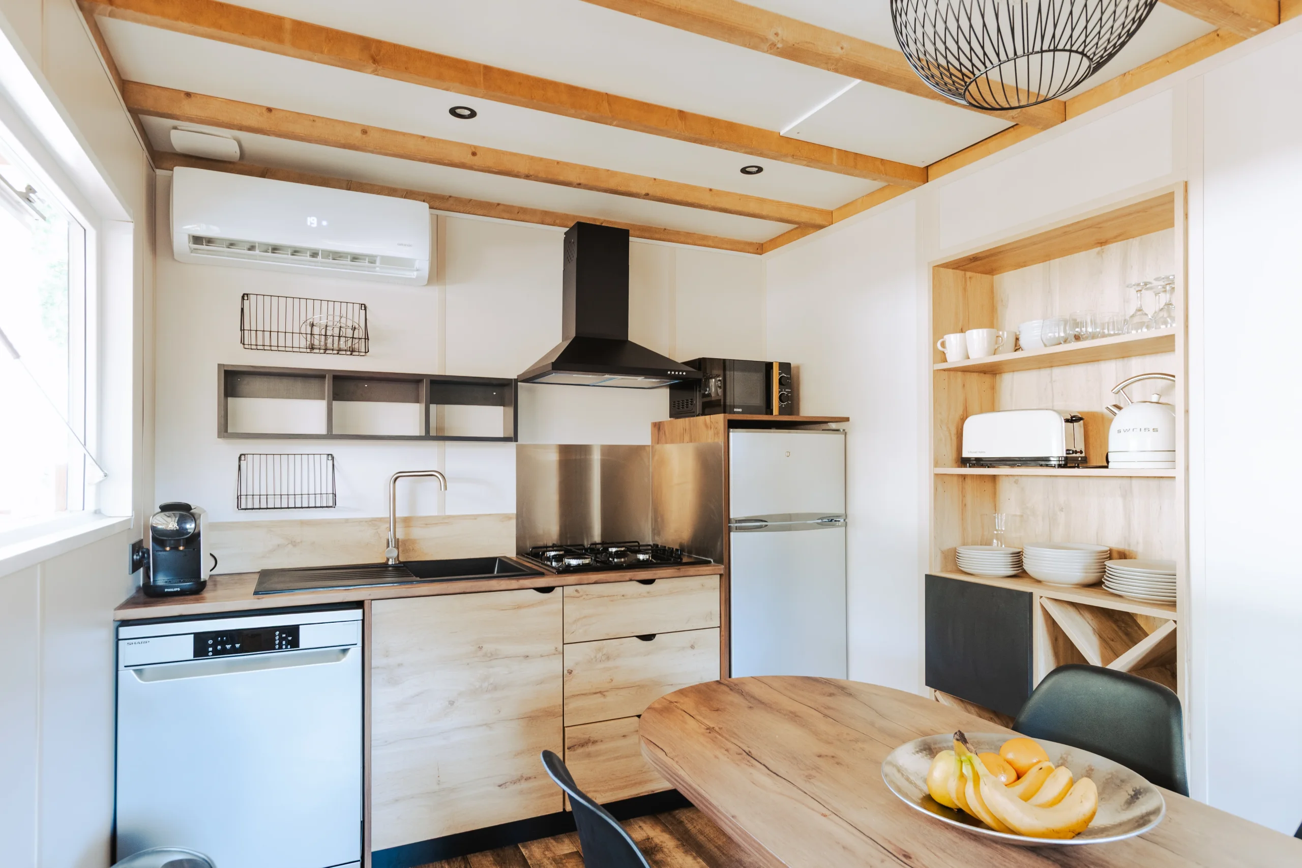 Cuisine avec plaques de cuisson, hotte, réfrigérateur et lave-vaisselle, à côté d’une table à manger.