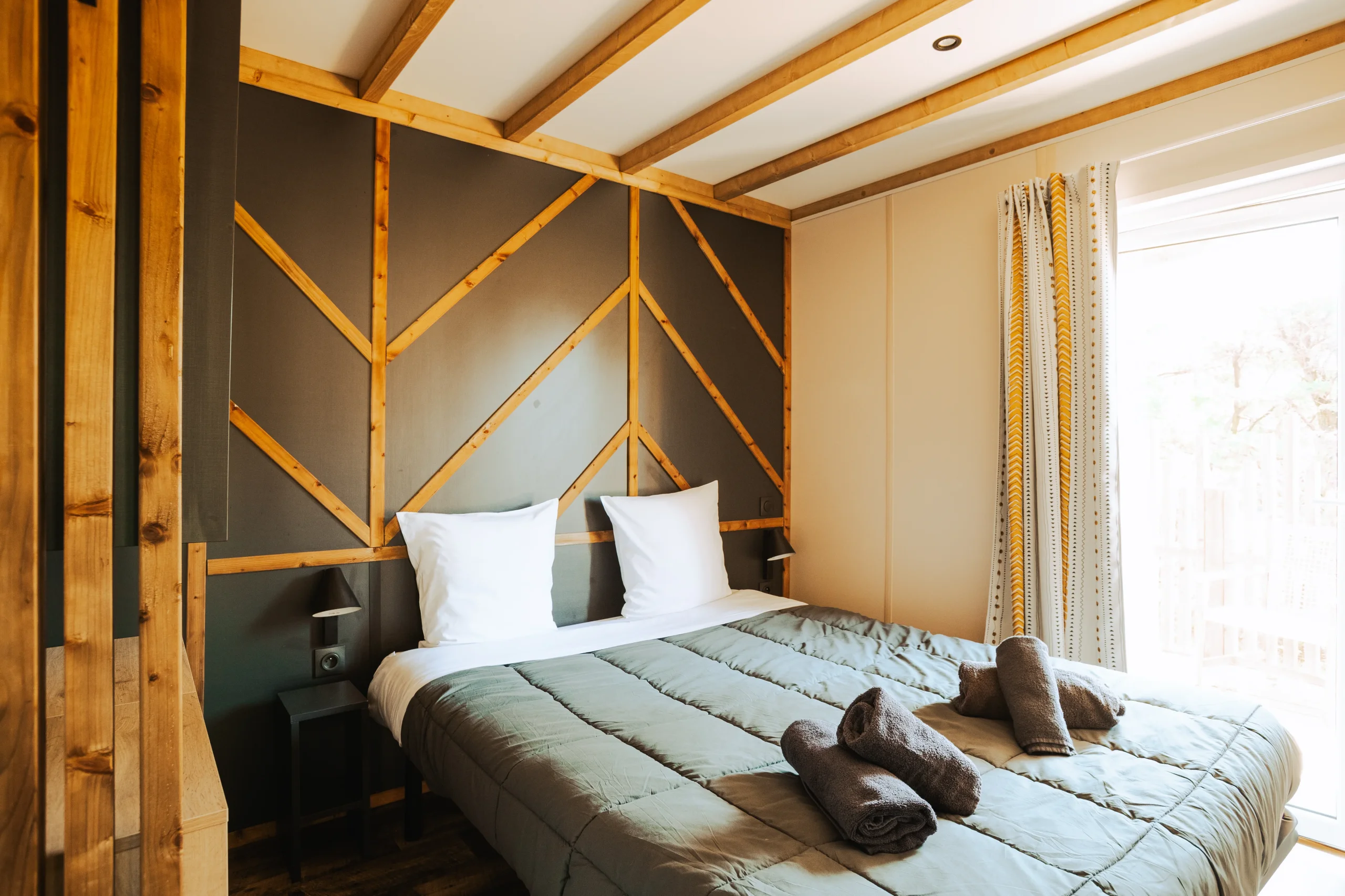 Chambre avec lit double et tête de lit aux motifs de bois dans un hébergement insolite vers Biarritz du Camping le ruisseau.
