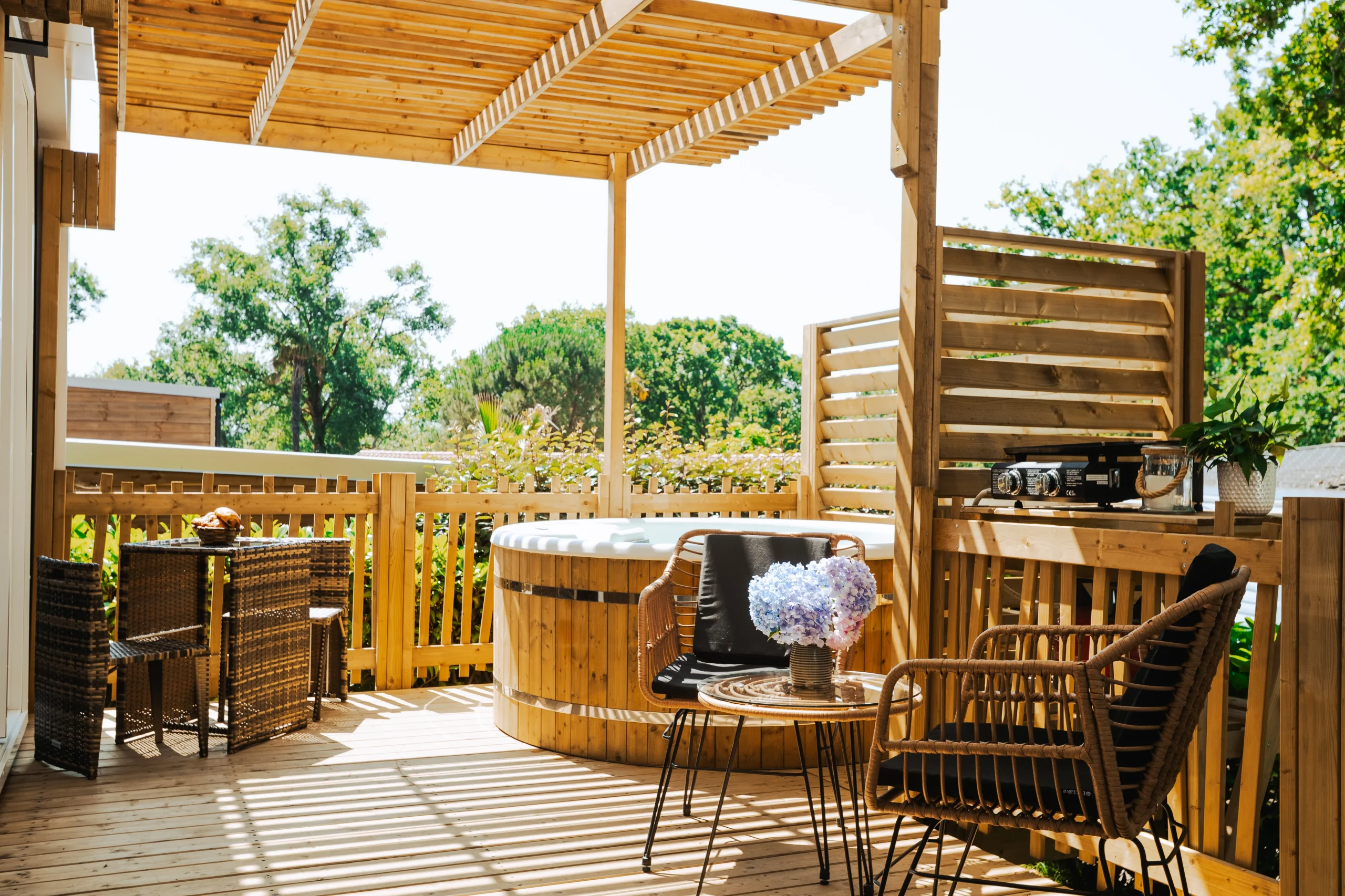 Terrasse d'un hébergement insolite vers Biarritz au Camping le ruisseau, avec bain extérieur rond et fauteuils sous une pergola.