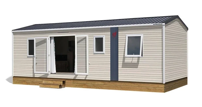 Mobil-home du Camping le ruisseau avec bardage clair, baie centrale ouverte et marches d’accès en bois.