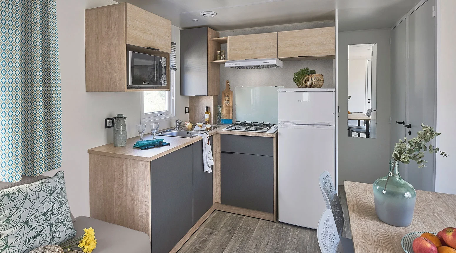 Cuisine en L avec évier, plaques de cuisson, réfrigérateur et micro-ondes, à côté du coin repas.