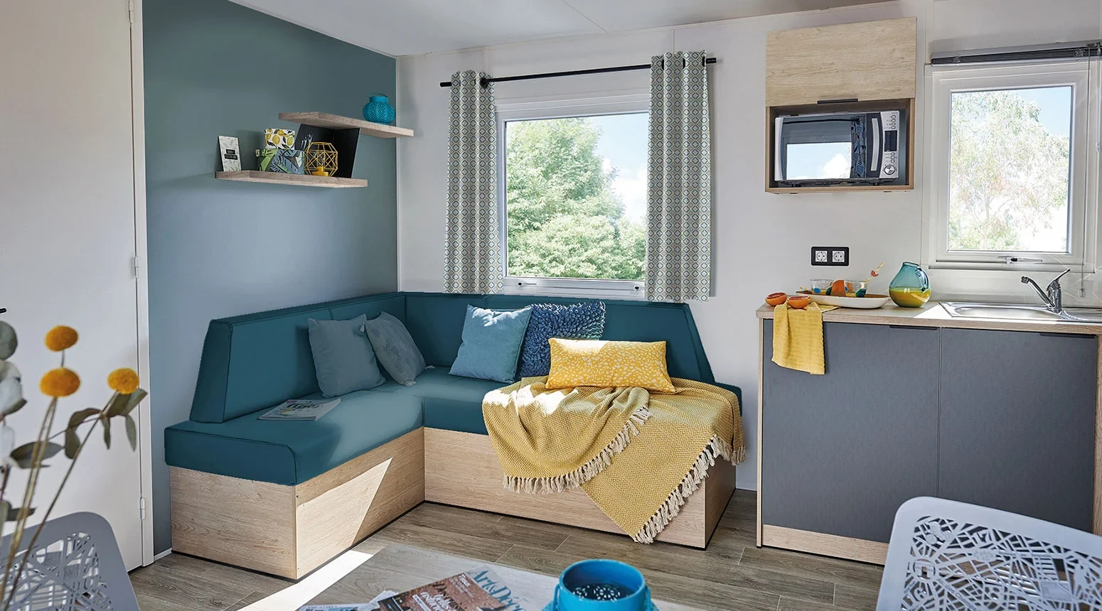 Salon avec banquette d’angle bleu pétrole et kitchenette d’un hébergement insolite vers Biarritz au Camping le ruisseau.