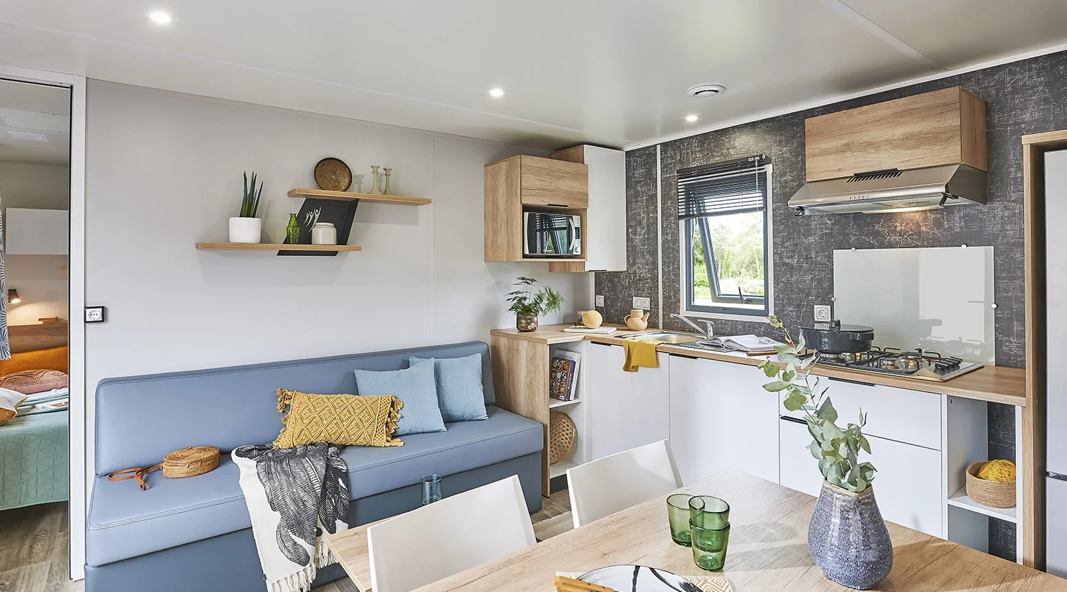 Pièce de vie avec banquette, table à manger et cuisine ouverte équipée.