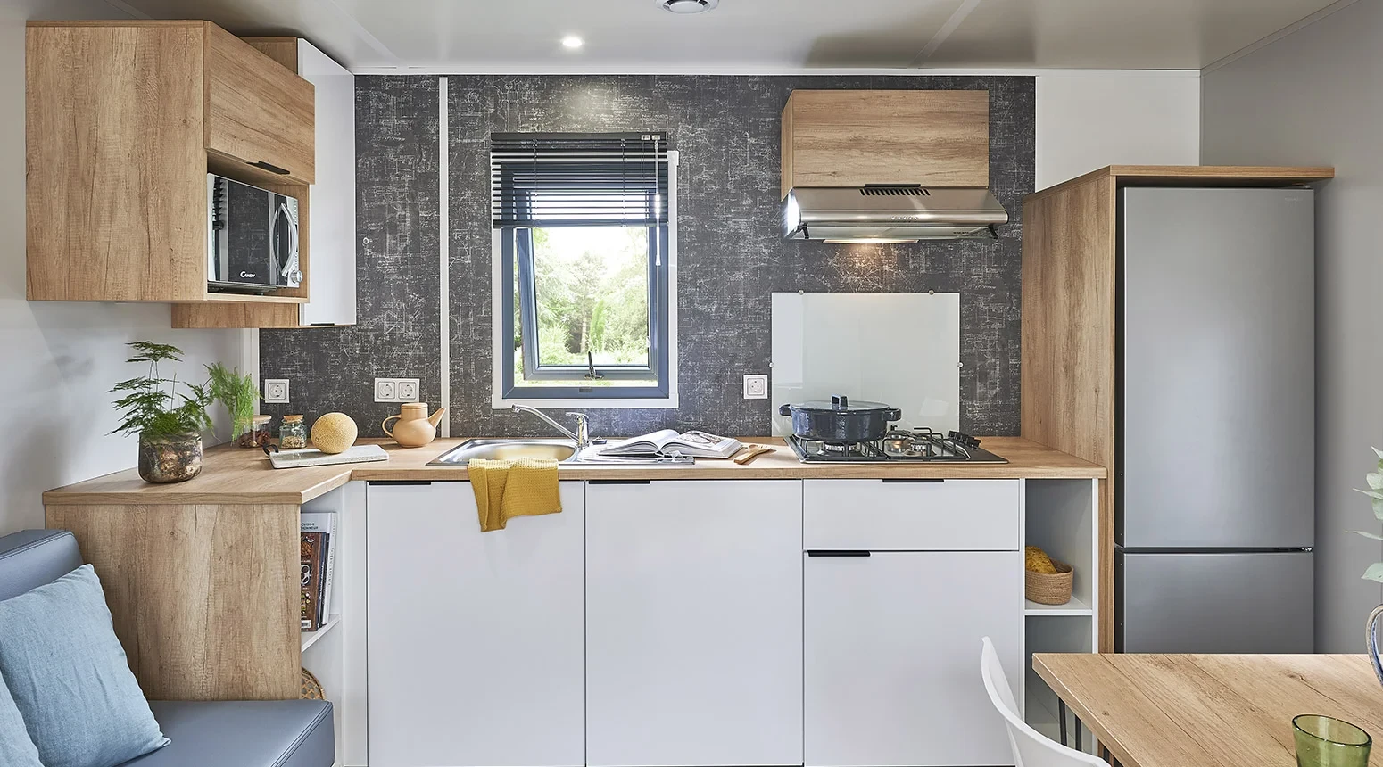 Cuisine avec évier sous la fenêtre, plaques de cuisson, micro-ondes et réfrigérateur avec compartiment congélateur.