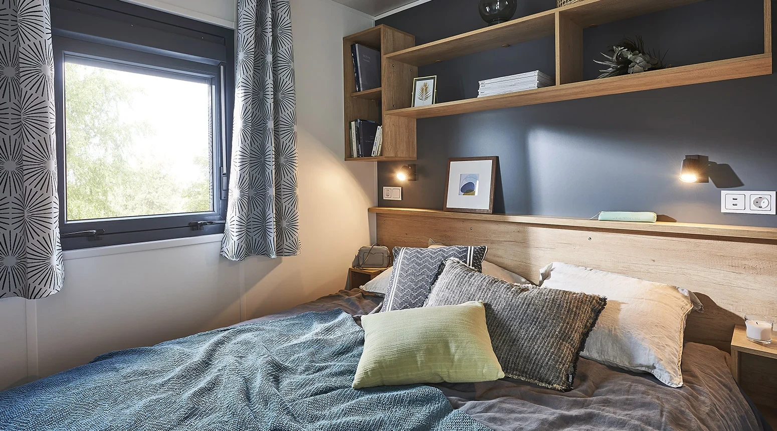 Chambre avec lit double, tête de lit en bois et liseuses au Camping le ruisseau.